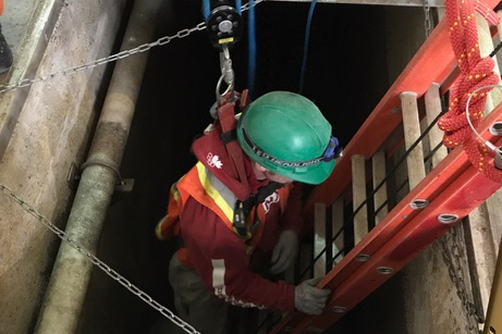 a rescue team lowering a point man wearing PPE and fall protection equipment into a confined space via a ladder.